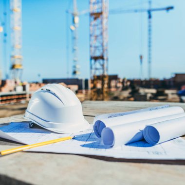 close-up shot of rolls of papers with building plans and hardhat at construction site clipart