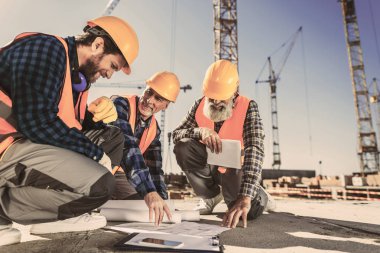 construction workers sitting on concrete at construction site and looking at building plans clipart