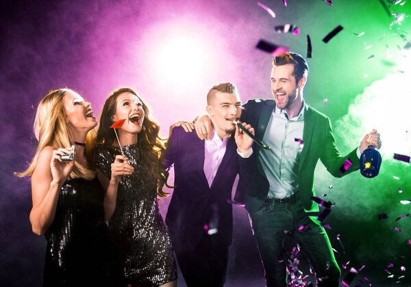 Group of happy friends having fun with champagne bottle and confetti