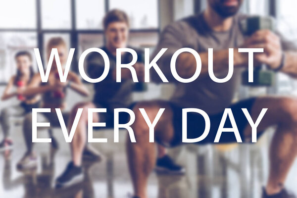 blurred group of athletic young people in sportswear with dumbbells exercising at gym, workout  every day inscription