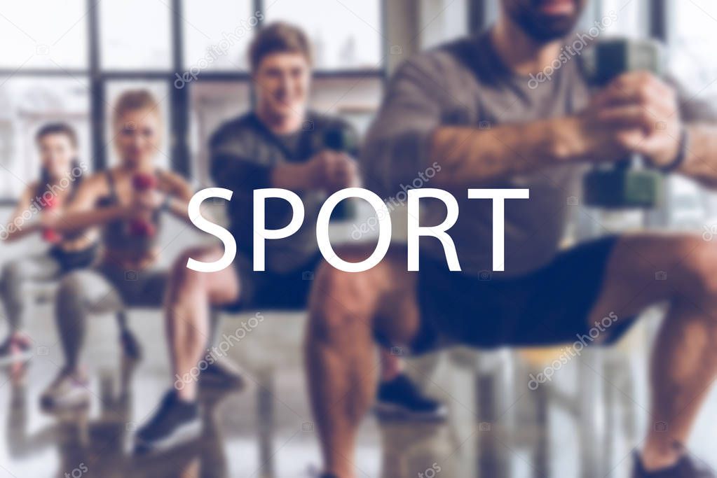 blurred group of athletic young people in sportswear with dumbbells exercising at gym, sport inscription