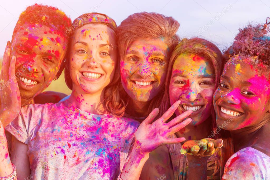happy young multiethnic friends having fun with colorful powder at holi festival and looking at camera