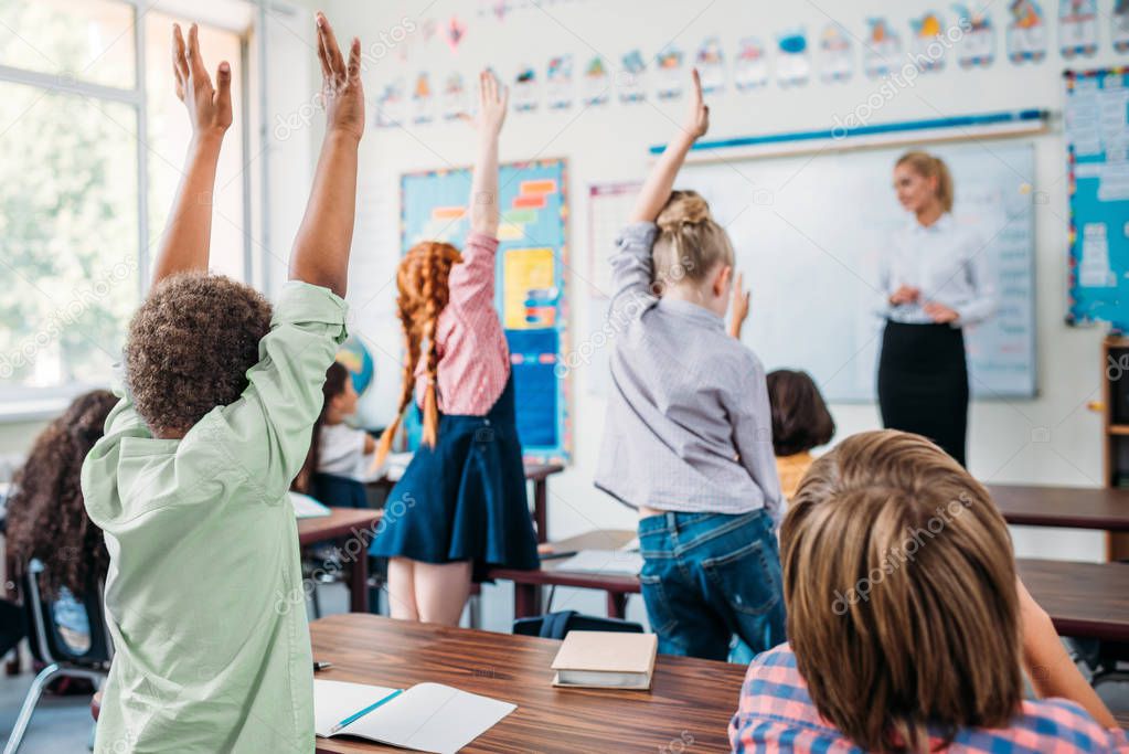 group of kids raising hands in class to answer teachers question