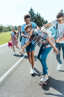 mutlu çok ırklı genç sınıf kaykay ve birlikte parkta yürüyüş ile eğleniyor