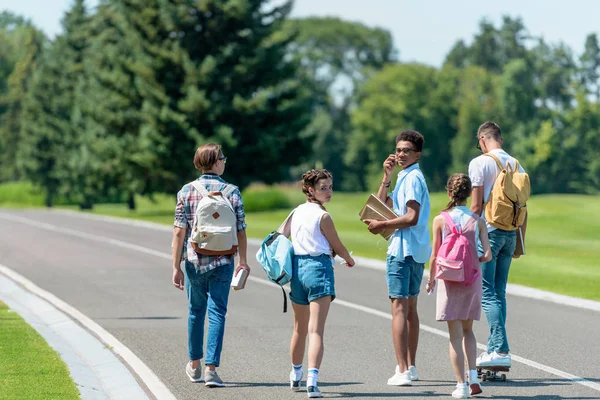 多民族の十代の友人本と公園を一緒に歩いてバックパックの背面図 — ストック写真