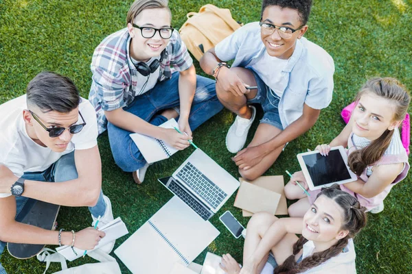 mutlu çok ırklı genç öğrencilerin kitap ve Park dijital cihazlar ile eğitim yüksek açılı görünüş