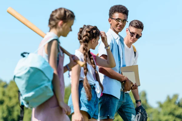 多民族青少年学生的侧面观与书籍 背包和运动器材一起漫步在公园里 — 图库照片