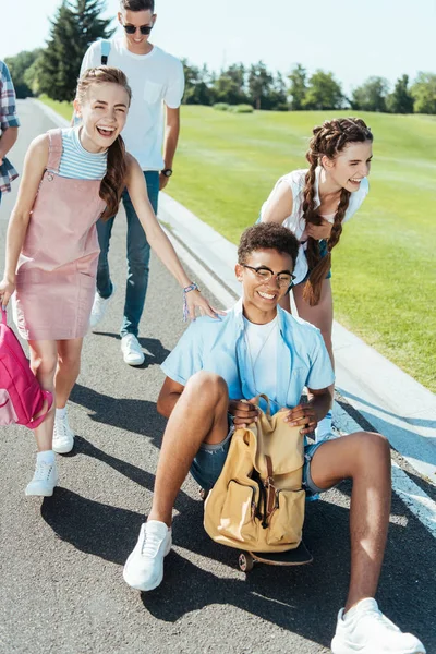 mutlu gençler ise Afro-Amerikan çocuk holding sırt çantası gülümseyen ve kaykay üzerinde oturan gülüyor