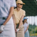 Selektiver Fokus der Frau mit Schirmmütze und Sonnenbrille beim Golfspielen auf dem Golfplatz