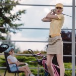 Selektiver Fokus der Golferin beim Golfspielen, während ihr Freund sich auf dem Golfplatz ausruht