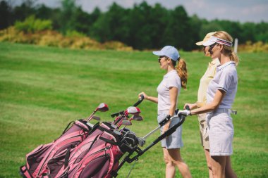 side view of female golfers with golf equipment walking at golf course clipart