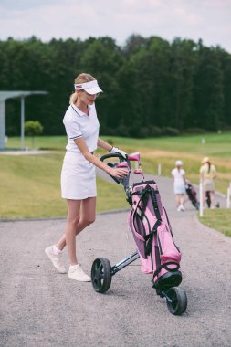 seçici odak kadın golf oyuncusu kap ve beyaz polo ile golf golf sahasında dişli