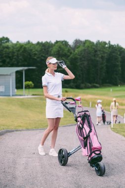 seçici odak kadın golf oyuncusu kap ve beyaz polo ile golf golf sahasında dişli