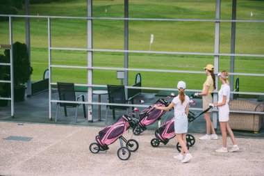 golf ile kadın golfçüler yan görünüm dişli golf sahasında yaz gününde yürüyüş
