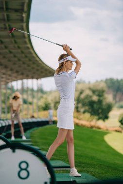 selective focus of smiling female golfer in polo and cap playing golf at golf course clipart