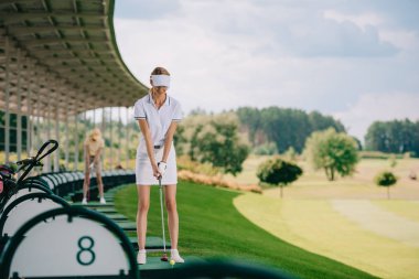 selective focus of smiling female golfer in polo and cap with golf club at golf course clipart