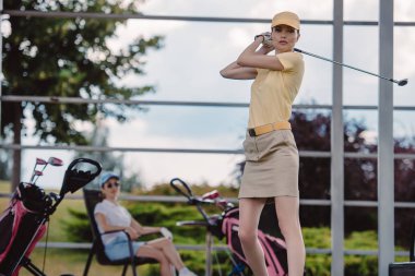kadın golf oyuncu oynarken golf golf sahasında arkasında oturan arkadaşı ise seçici odak