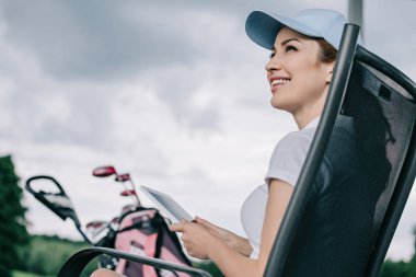 şapkalı neşeli kadın golf oyuncusu tablet ellerde ile düşük açılı görünüş