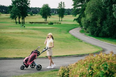 kadın golf oyuncu golf sahasında yürürken smartphone üzerinde konuşurken golf dişli ile yan görünüm