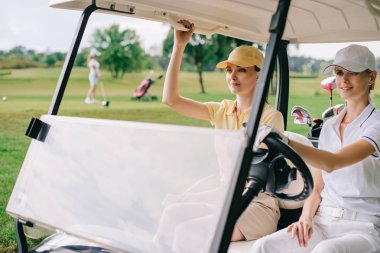 golf sahasında golf arabası sürme kapaklar kadın golfçüler gülümseyen