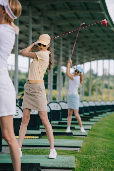 selective focus of female golf player with golf clubs playing golf at golf course