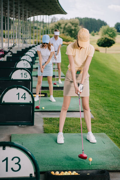 selective focus of women in caps with golf clubs playing golf at golf course