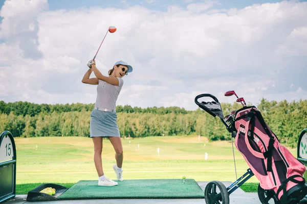 side view of woman in polo and cap playing golf at golf course