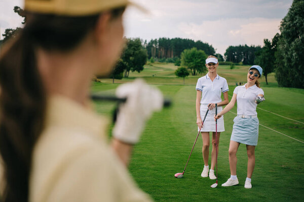 selective focus of smiling women with golf clubs at golf course