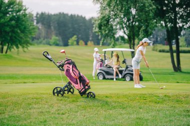 seçici odak olan kadın golf kulübü golf ve golf arabası yeşil çimenlerin üzerine oturan arkadaşlar