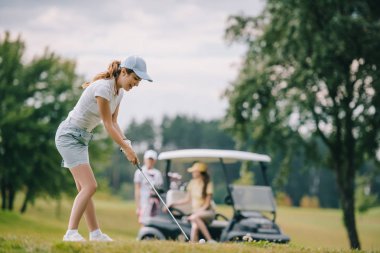 seçici odak olan kadın golf kulübü golf ve golf arabası yeşil çimenlerin üzerine oturan arkadaşlar