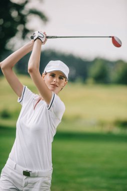 portrait of female golf player in cap with golf club in hands at golf course clipart