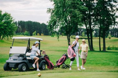 group of female golf players in caps with golf equipment at golf course on summer day clipart