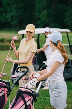 kadın golf oyuncu golf ekipmanları ve golf arabasında yeşil çim arkadaşıyla seçici odak