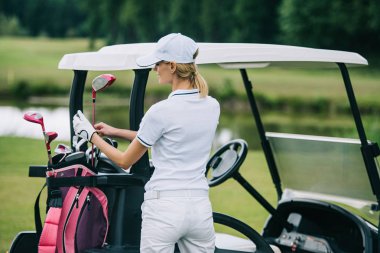 Arkadan Görünüş polo ve golf dişli golf sahasında golf arabası yaz günü ayakta ile kap içinde kadın