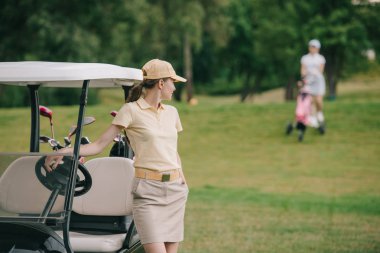golf arabası yeşil çim üzerinde şapkalı kadın golf oyuncu seçici odak