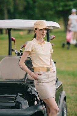 seçici odak ile şapkalı kadın golf oyuncusu ceplerinde golf arabası yeşil çim üzerinde eller