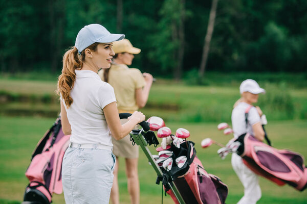 selective focus of women in caps with golf gear walking on green lawn at golf course