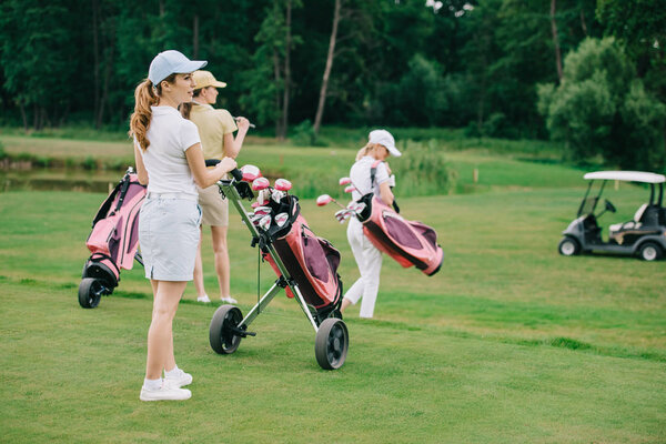selective focus of women with golf gear walking on green lawn at golf course