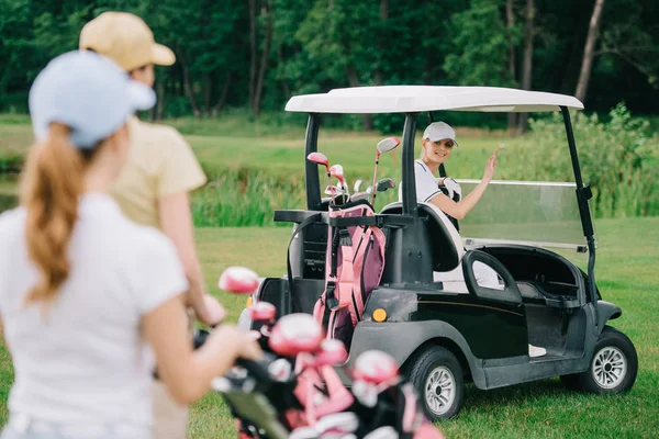 selective focus of woman in golf cart greeting friends at golf course