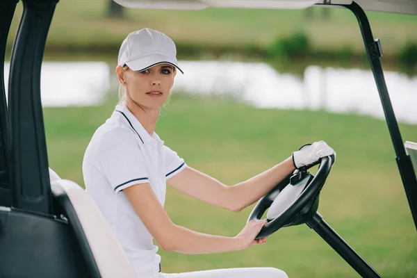 高尔夫球场中的女子帽和马球骑高尔夫球车的侧面视图 — 免费的图库照片