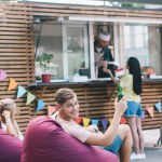 Lächelnder Mann mit Bierflasche in der Nähe eines Foodtrucks und Blick in die Kamera