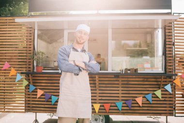 young small business owner standing with crossed arms and smiling at camera near food truck clipart