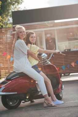 Gıda kamyon yakınındaki kırmızı scooter üzerinde oturan ve kameraya bakarak kız gülümseyerek