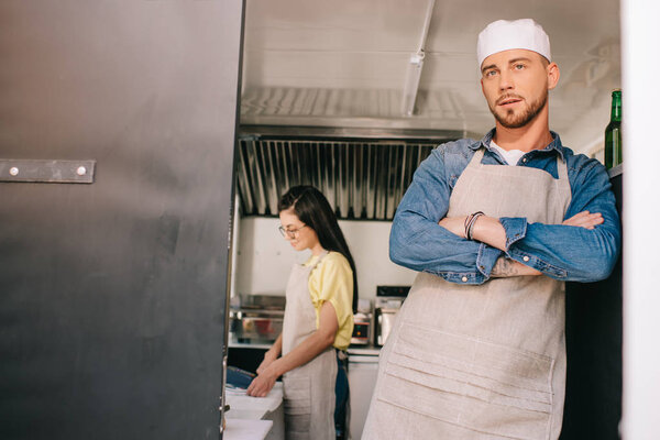 male chef standing with crossed arms while female colleague working behind in food truck