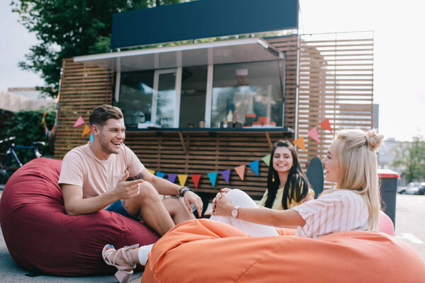 happy young friends talking while sitting on bean bag chairs near food truck 