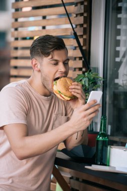 man eating burger and using smartphone at food truck clipart