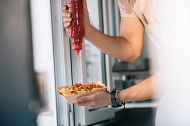 cropped image of chef adding ketchup to hot dog in food truck clipart