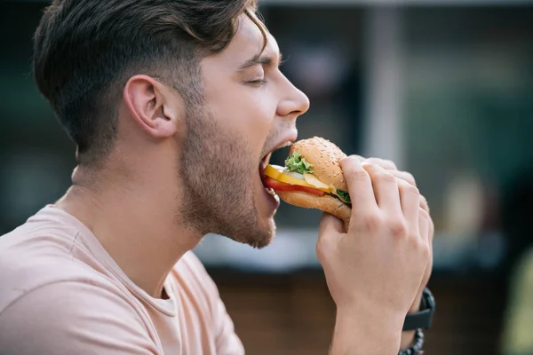 Widok Boku Człowieka Jedzenie Smaczne Burger Zamkniętymi Oczami — Zdjęcie stockowe