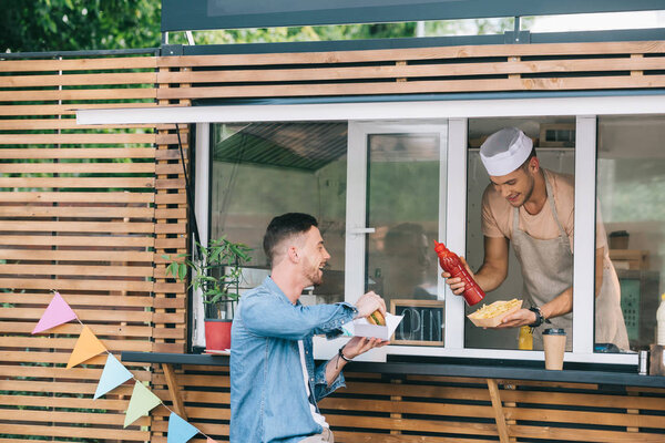 chef giving hot dog and ketchup to customer from food truck