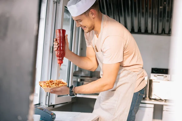 厨师在食品卡车中添加番茄酱给热狗的侧面视图 — 图库照片